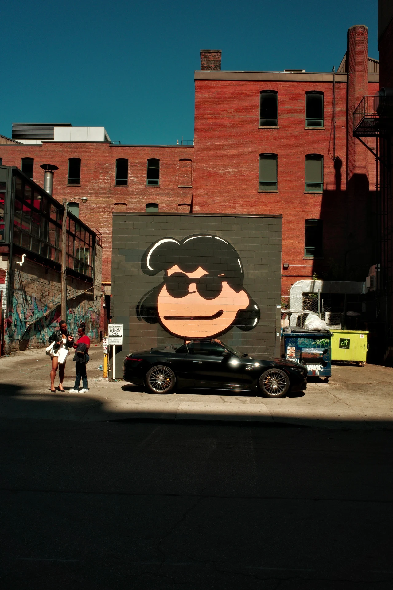 A Lucy mural, a parked car and two people in afternoon light