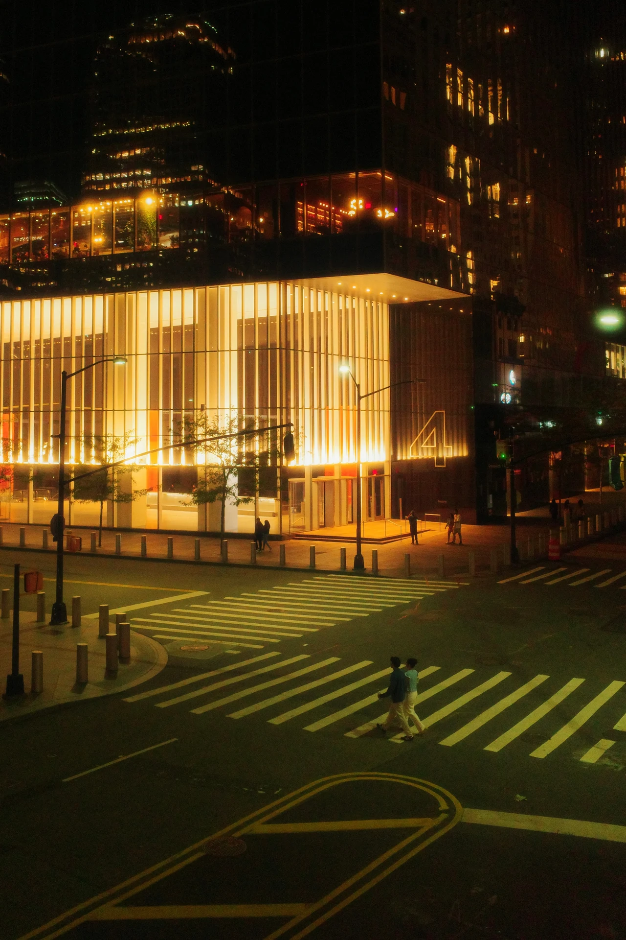 Two people crossing beneath a glowing building at night