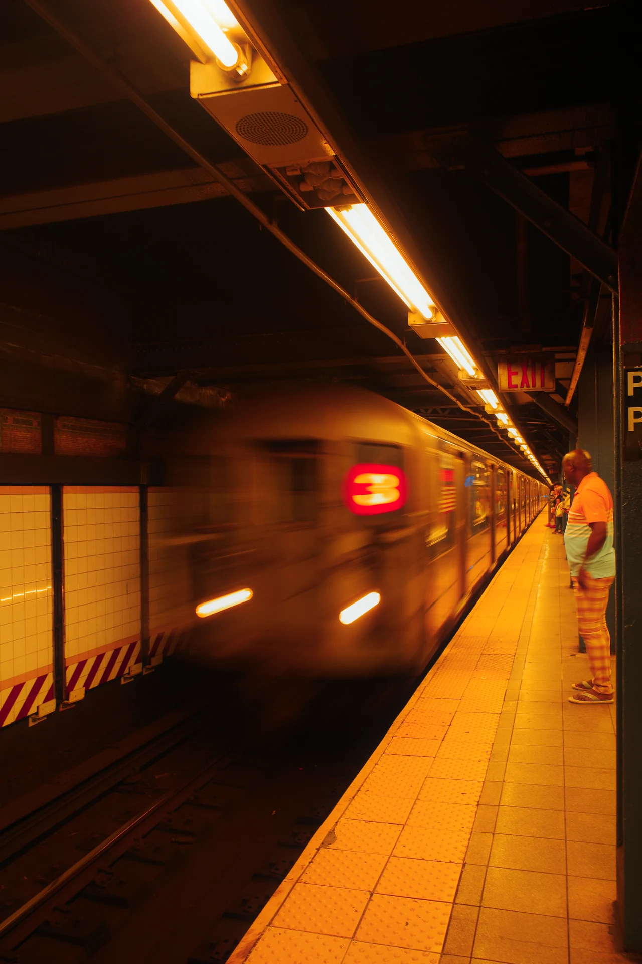 A moving subway train under amber platform lights